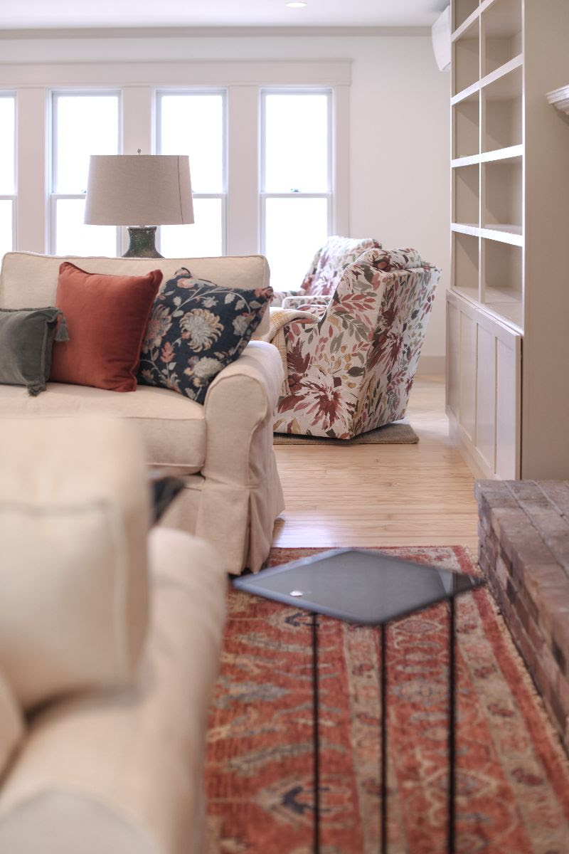 Living room with sofa and swivel chairs in a floral pattern. Beautiful lighting, bookshelf, and the hint of a fireplace.